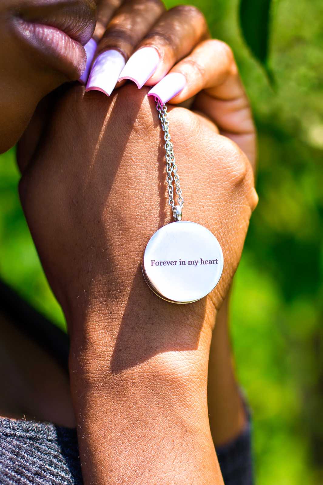Black woman holding onto the lovely Paw Print Memorial Locket to memorialize your beloved pet and safely store their ashes for you to cherish forever.