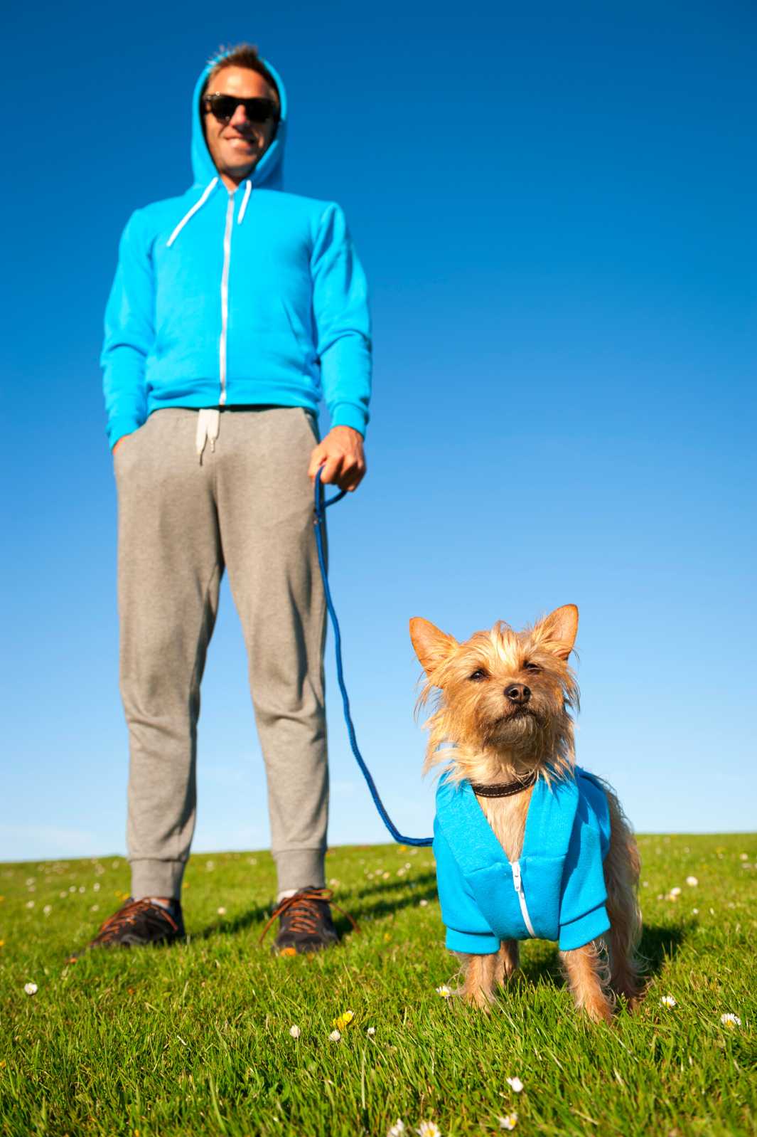 Dog owner and their small dog standing outside on a blue sky summer day, wearing matching blue zip up hoodies.