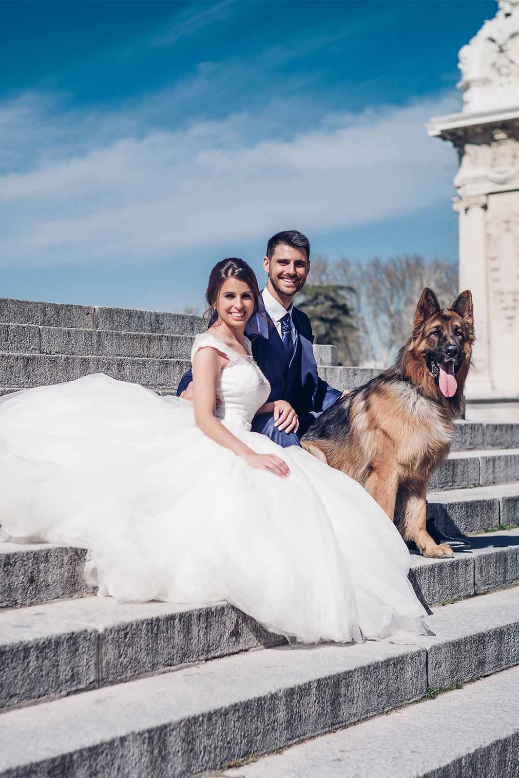 Young smiling newlyweds sitting with their dog on the church steps.