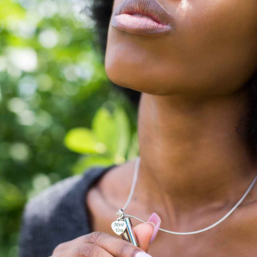 Black woman holding up the beautiful silver Miss You Memorial Urn Necklace from online keepsake jewelry they made me wear it.
