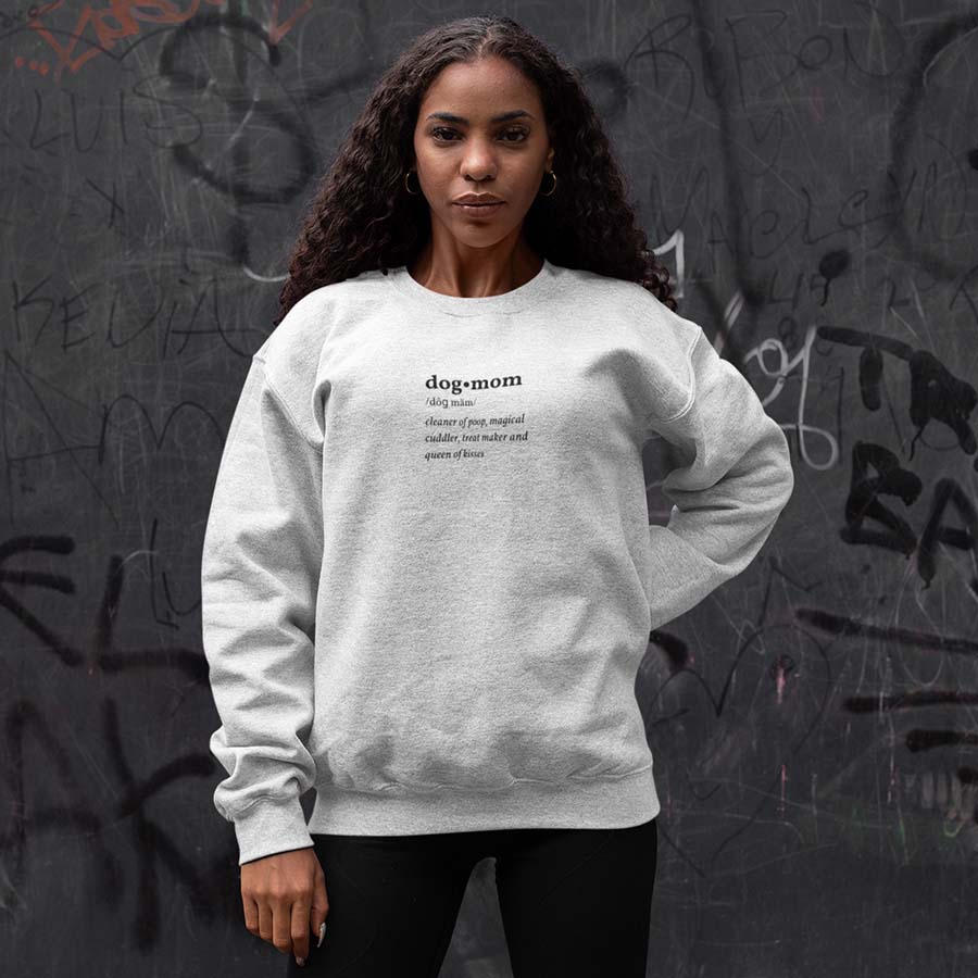 Woman standing against graffiti wall wearing Oatmeal Dog Mom Defined Crewneck Sweatshirt from online outerwear and activewear clothing store for pet parents, they made me wear it.