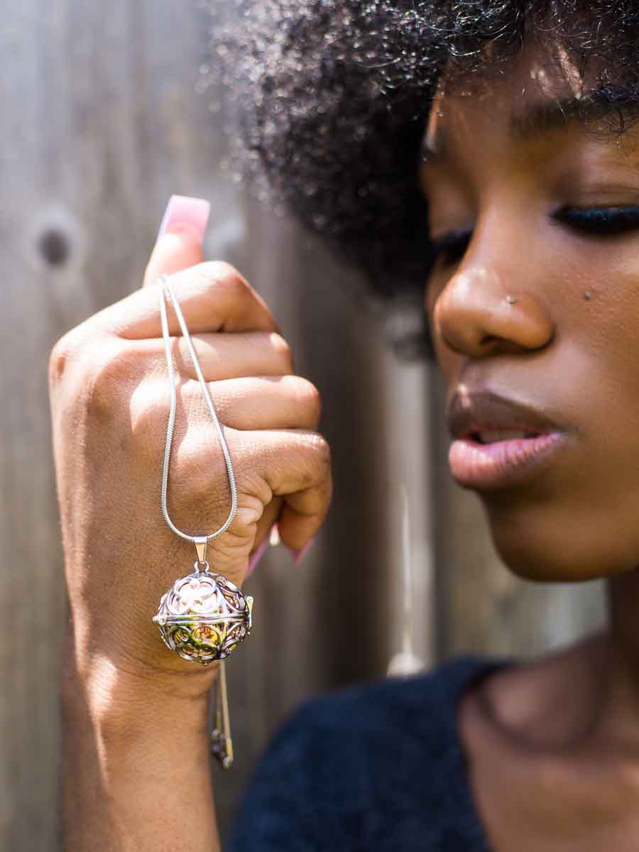 Black woman holding up beautiful keepsake jewelry, Hollow Ball Steampunk Memorial Urn Necklace in Rose Gold from online boutique they made me wear it.