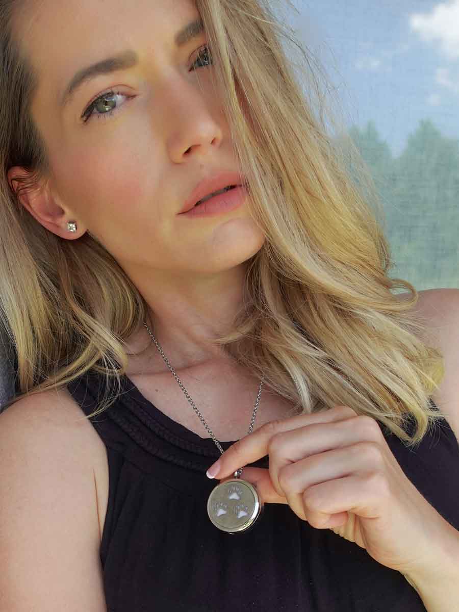 Woman wearing the beautiful Silver Paw Print Memorial Locket. The perfect bereavement gift for family and friends who want a cremation locket to hold a small amount of pet ashes to remember their dog who crossed over the rainbow bridge. The locket can also be used as an aromatherapy essential oil diffuser as it comes with 12 free felt pads. Available from online boutique store they made me wear it.