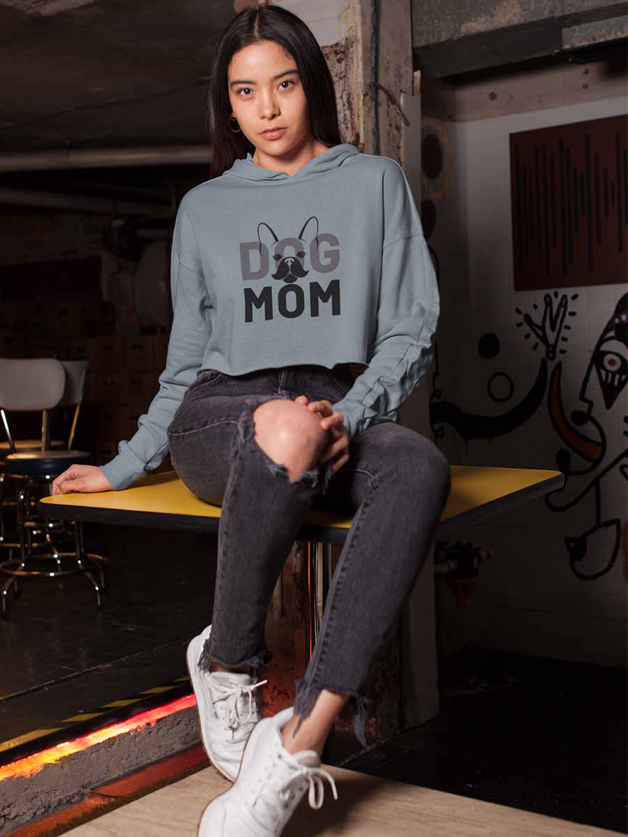 Young woman sitting on a table, wearing the Sage Dog Mom Cropped Hoodie from online outerwear and activewear clothing store for pet parents, they made me wear it.